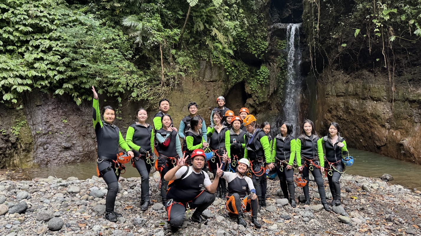 Group of Canyoning participants posing in front of a waterfall in Bali after completing an exciting canyoning adventure through canyons.
