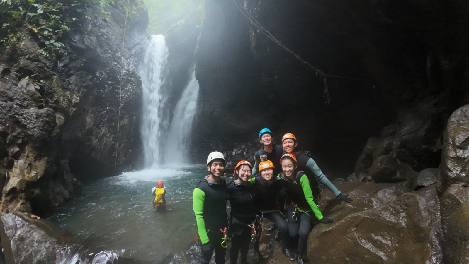 Group of Canyoning participants posing in front of a waterfall in Bali after completing an exciting canyoning adventure through canyons.
